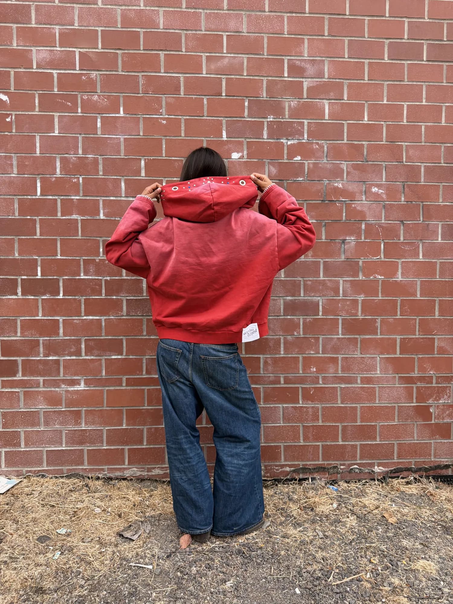 Back view of a model holding up the jeweled hood of the red Warlock Hoodie