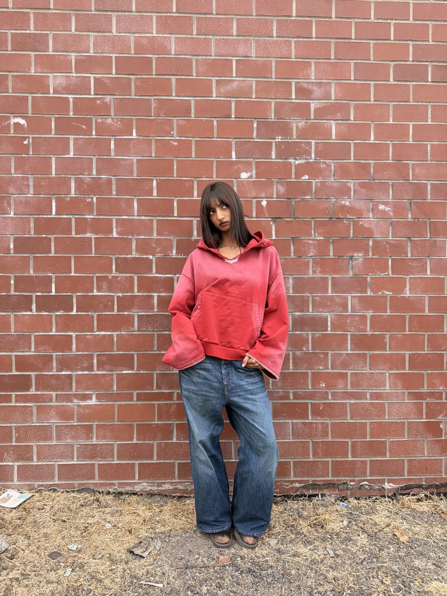 Model wearing the red Warlock Hoodie against a brick wall